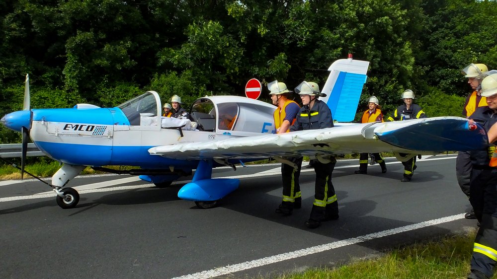 Feuerwehrleute packen gemeinsam an, um ein Flugzeug von der Autobahn zu einem Rastplatz zu schieben.