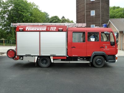Das LF10 des Löschzuges St. Vit steht auf einer asphaltierten Fläche. Im Hintergund ist der Schlauchturm der Kreisfeuerwehr in St. Vit zu erkennen.